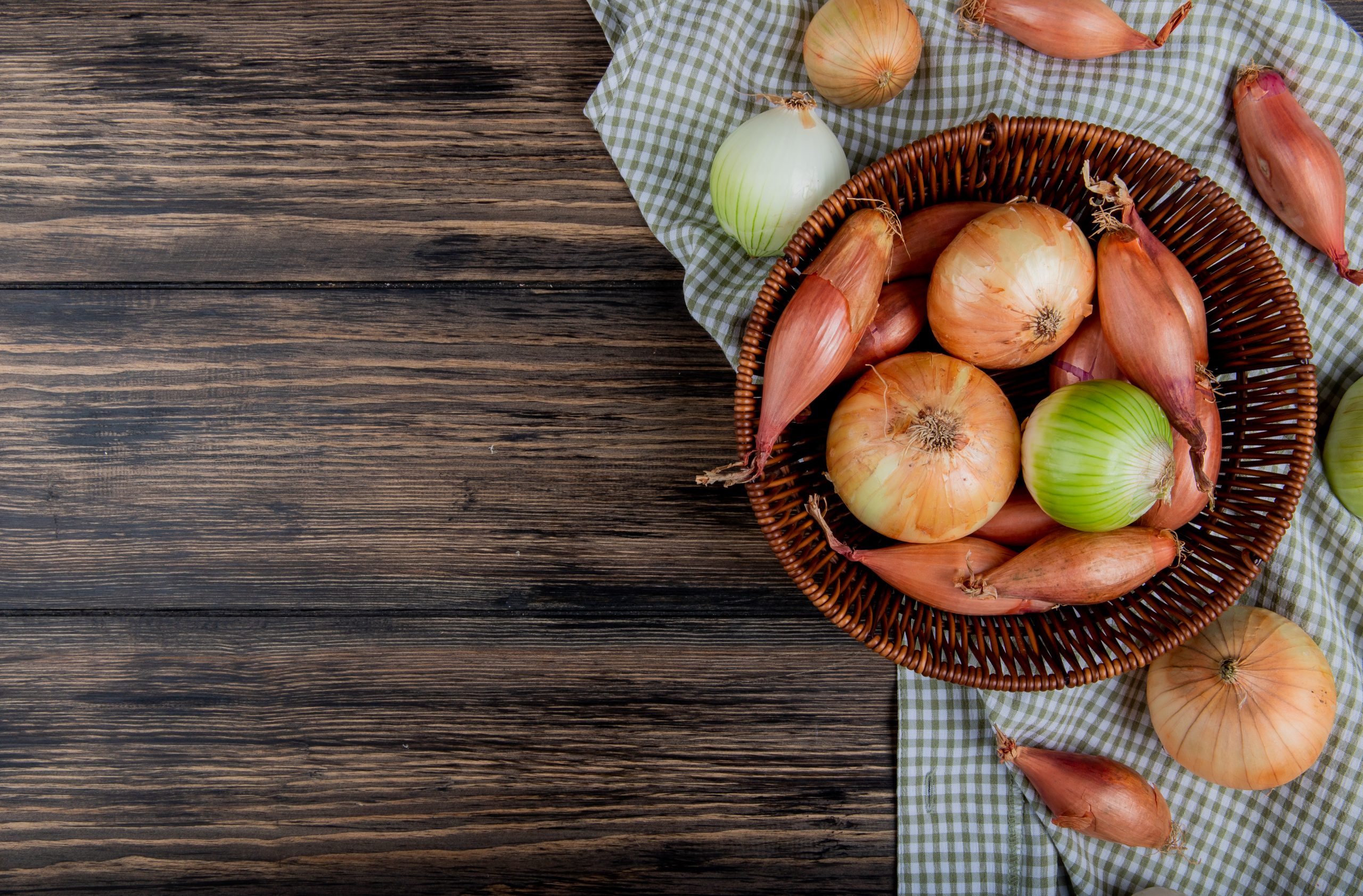 top view of onions as shallot sweet and white ones in basket on plaid cloth and wooden background with copy space